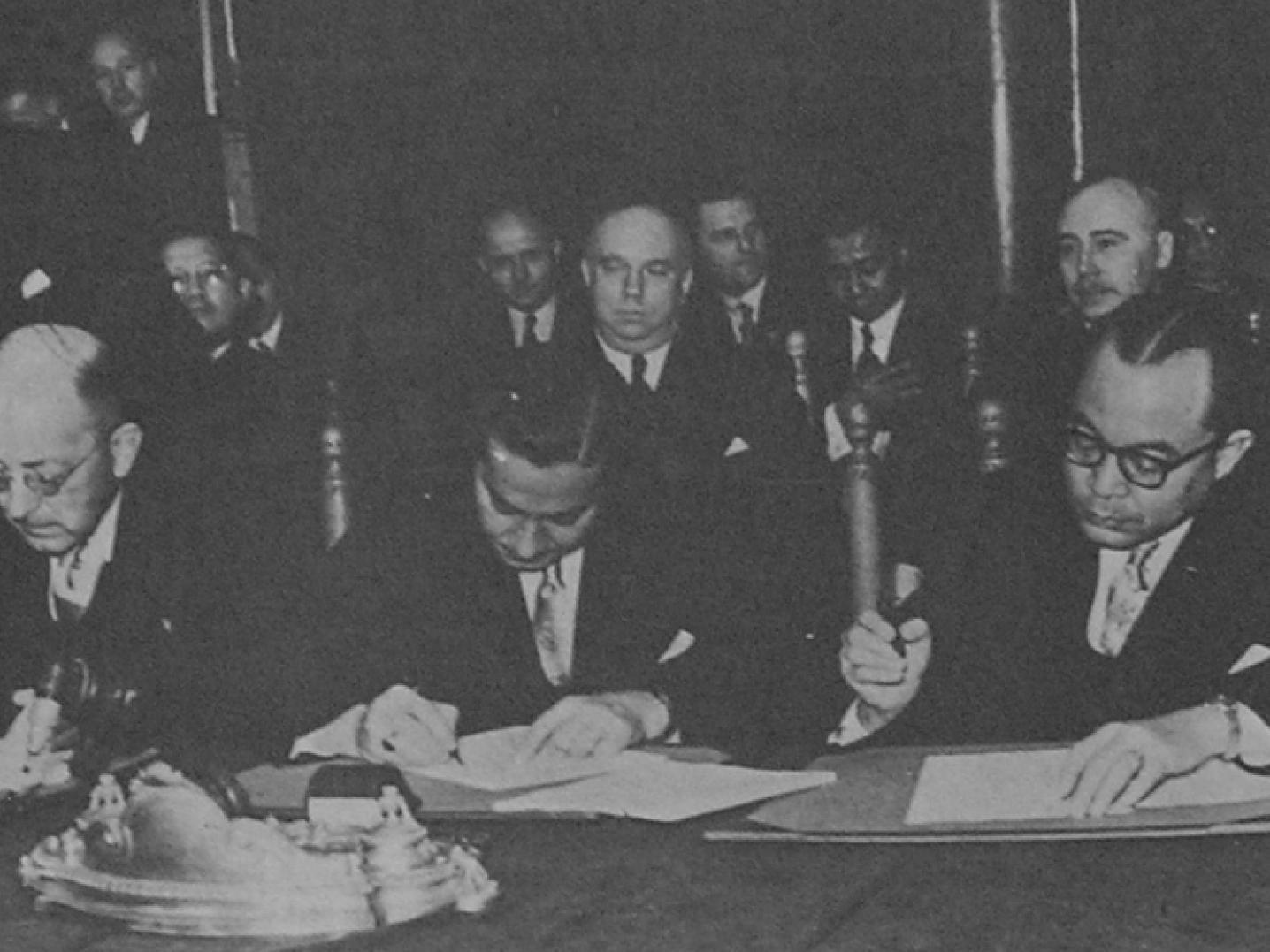 a group of Dutch and Indonesian men signing a paper during the Dutch-Indonesian Round Table Agreement in 1949