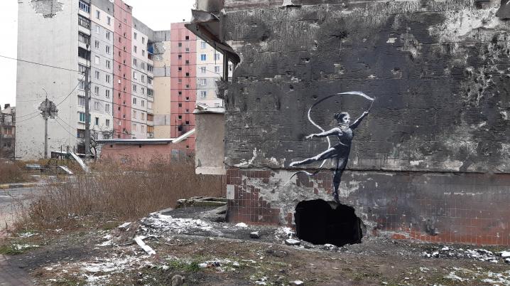 a graffiti on a shelled building in Irpin, Ukraine, of a woman in a leotard and a neck brace waving a ribbon